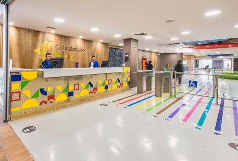 Ingreso a BLOC Plaza de las Américas muestra la recepción, logos, líneas coloridas y personas.