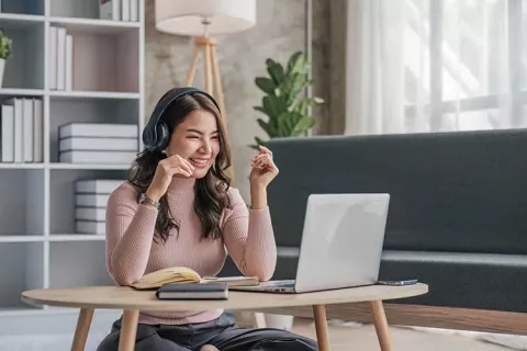 Mujer estudia bachillerato flexible por ciclos Colsubsidio con audífonos, libros y laptop desde casa.