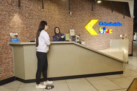 BLOC Ricaurte Colsubsidio muestra 2 mujeres hablando en la recepción, pared de ladrillo y el logo.