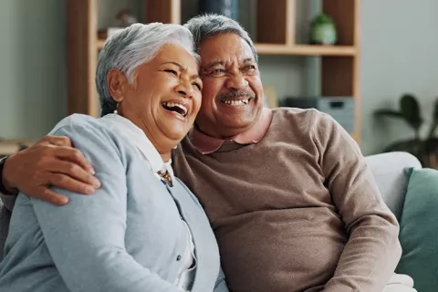 Pareja de pensionados se abrazan en la sala de su vivienda 