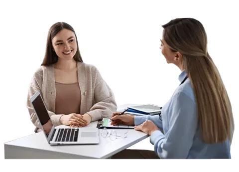 Dos mujeres sentadas en un escritorio hablando.