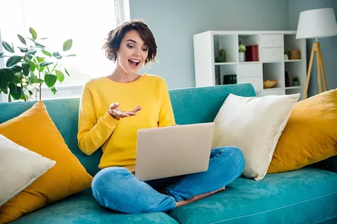 Mujer sonríe viendo pantalla de un computador portátil