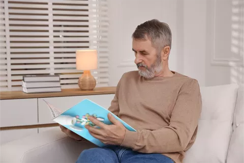 Una hombre sentado en su sofá hojea la Revista Vida Sana de Colsubsidio
