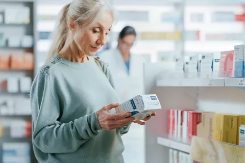 Mujer mayor viendo un medicamento cerca de un estante