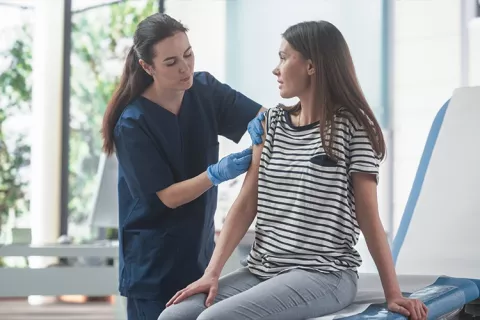 Enfermera vacuna a una joven en centro médico.