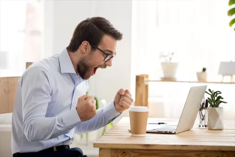 Hombre sorprendido al frente de su portátil al ver los paquetes especiales de Colsubsidio.