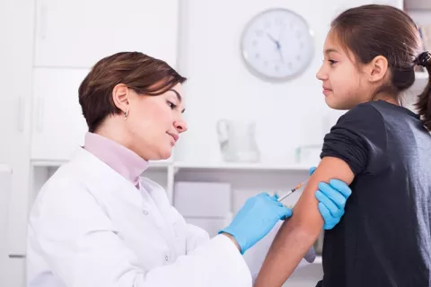Médica vacuna a una niña en consultorio médico.