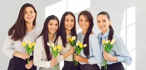 5 mujeres sosteniendo flores y felices.
