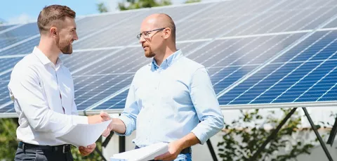 Dos adultos dándose la mano y de fondo páneles solares.