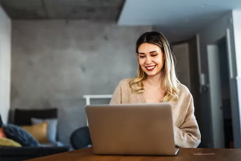 Mujer feliz en su portátil por recibir crédito estudiantil con Colsubsidio