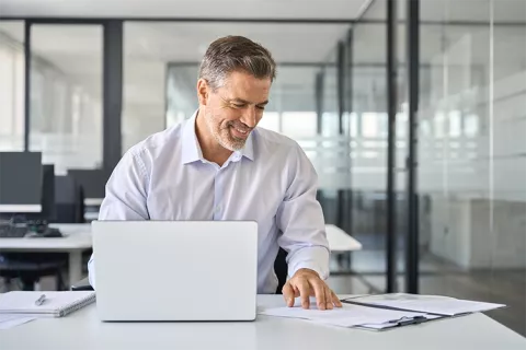 Hombre aprendiendo de finanzas, estudiando en su portátil y apuntes