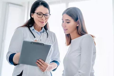 Mujer en control médico y su doctora explicando tratamiento.