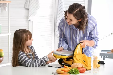 Mamá empacando la lonchera de su hija en la maleta.