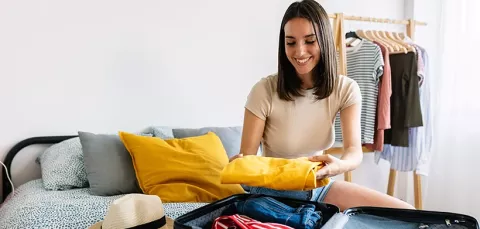 Mujer feliz empacando su maleta para su próximo viaje con Colsubsidio.