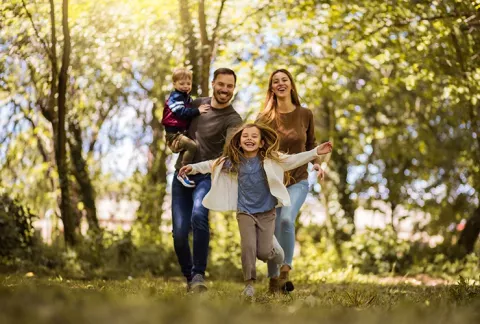 Una familia corre feliz y disfruta del sol en la zona campestre del Club Bellavista Colsubsidio.
