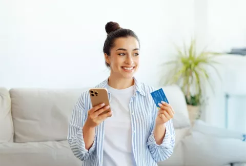 Mujer sonriendo mientras sostiene tarjeta Colsubsidio y celular.