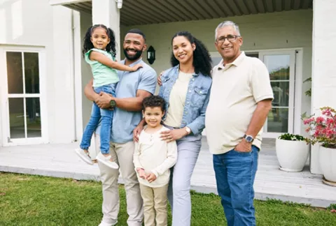  Familia y adulto mayor sonríen en su jardín. Esta familia está afiliada a Colsubsidio.