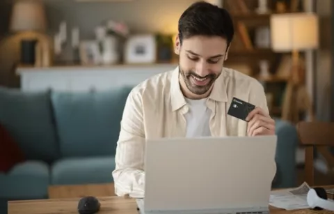 Hombre en la sala de su casa, al frente de su portátil, pagando en línea con la tarjeta Colsubsidio.