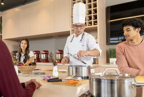 Grupo de personas aprendiendo del chef que esta preparando el menu