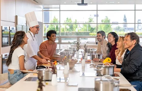 Compañeros de trabajo escuchando al chef, en un taller de cocina para empresas en BLOC Fontanar Colsubsidio.