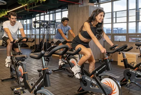 Tres personas entrenando en bicicleta estática en el gimnasio Colsubsidio.