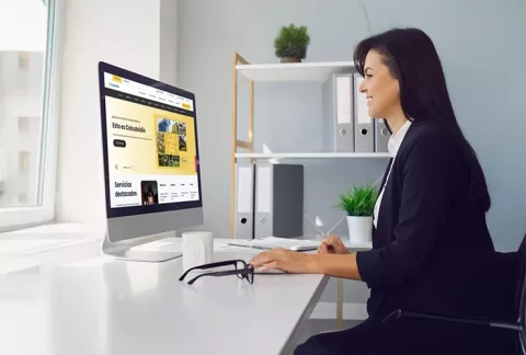 Mujer al frente de su computador navegando la página web de Colsubsidio.