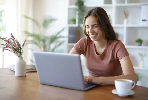 Trabajadora en su portátil feliz accede a la biblioteca digital para empresas de Colsubsidio