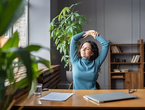 Mujer en su puesto de trabajo realiza estitamientos y pausas activas.