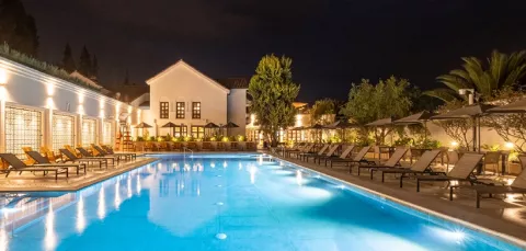 Piscina de los Hoteles Colsubsidio muestra sillas asoleadoras, zonas verdes, edificio blanco.