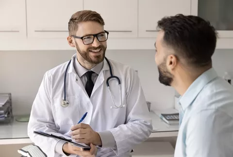 Doctor realiza examen de medicina preventiva a hombre joven, desde consultorio.