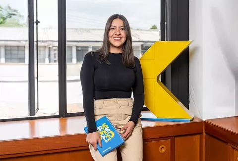 Joven sonríe y sostiene un cuaderno de Colsubsidio.