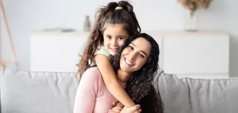 Madre e hija sonríen en la sala de su casa.