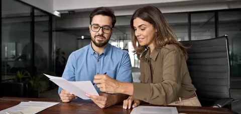 Hombre lee las condiciones crediticias que le presenta la asesora bancaria.