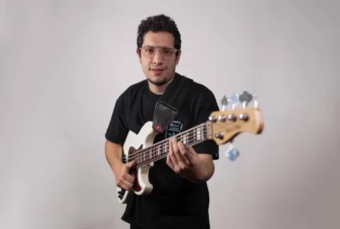 Un hombre sosteniendo una guitarra en sus manos mientras estaba parado frente a una pared blanca