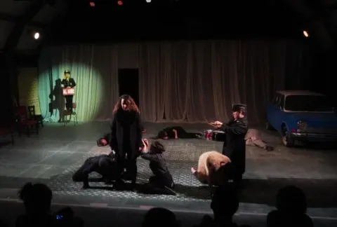 Varias personas vestidas con túnicas negras actúan en el escenario con un hombre vestido con una túnica negra