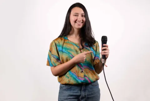 Mujer sosteniendo un micrófono y sonriendo mientras está de pie contra un fondo blanco.