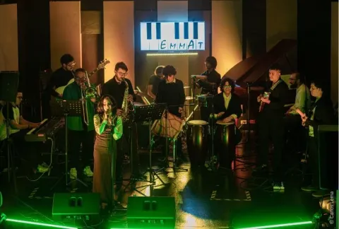 Banda tocando en una habitación con poca luz y un letrero de neón