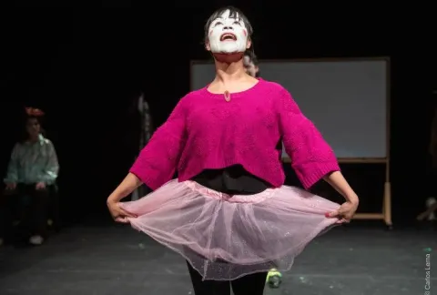 Mujer con un suéter rosa y tutú con una cara de payaso pintada en la cara.