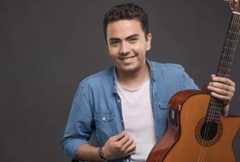 Hombre sosteniendo una guitarra y sonriendo a la cámara