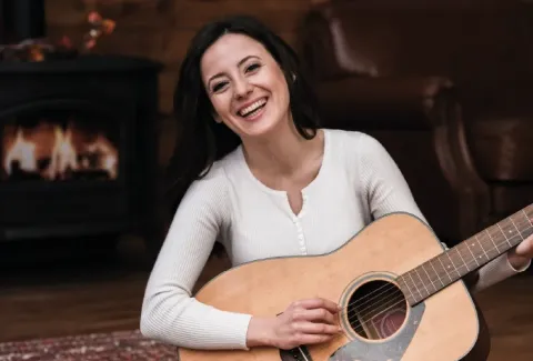Mujer sentada en el suelo con una guitarra sonriendo