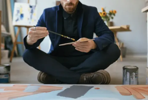 Hombre sentado en el suelo pintando un cuadro sobre un lienzo
