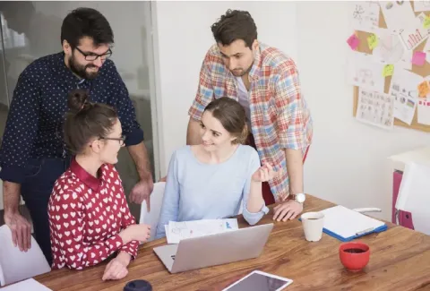 Varias personas están reunidas alrededor de una mesa con una computadora portátil y una tableta