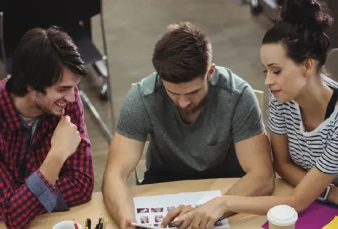 Tres personas sentadas en una mesa mirando una revista
