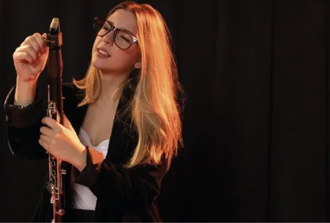 Mujer con gafas sosteniendo un clarinete delante de un fondo negro