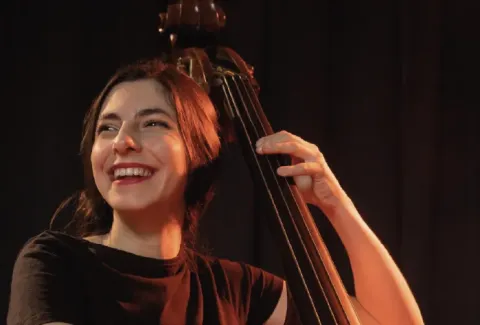 Mujer sosteniendo un bajo en su mano derecha y sonriendo