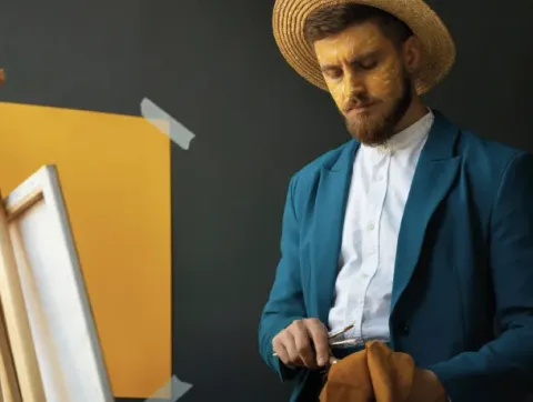 Un hombre con sombrero y traje azul está pintando sobre un lienzo.