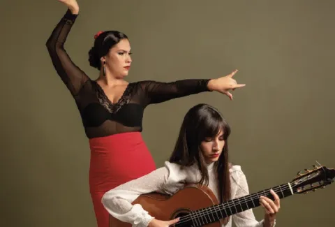 Mujer con falda roja y top negro tocando una guitarra.
