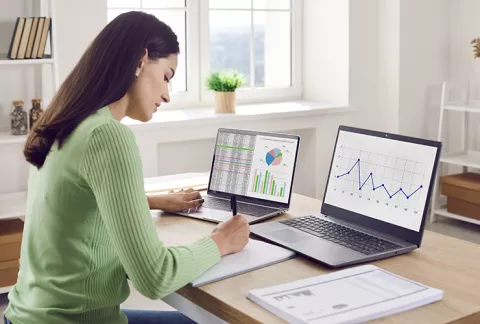 Mujer trabajando en un computador con gráficas de datos en la pantalla, curso Data Fundamentals.