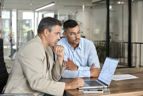 Asesor y empresario trabajando juntos frente a un computador, beneficio Alistamiento a la Medida.