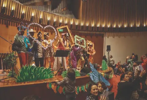 Presentación en el Teatro Colsubsidio con artistas en coloridos vestuarios y marcos decorativos.